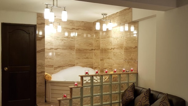 A modern bathroom with a bathtub, a glass partition, and a seating area with a sofa and cushions. - La Cabaña Hotel (Cusco)