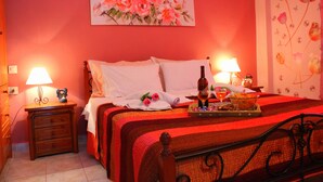 A hotel room with a bed, two bedside tables with lamps, a painting on the wall, and a floral wallpaper on the right wall.