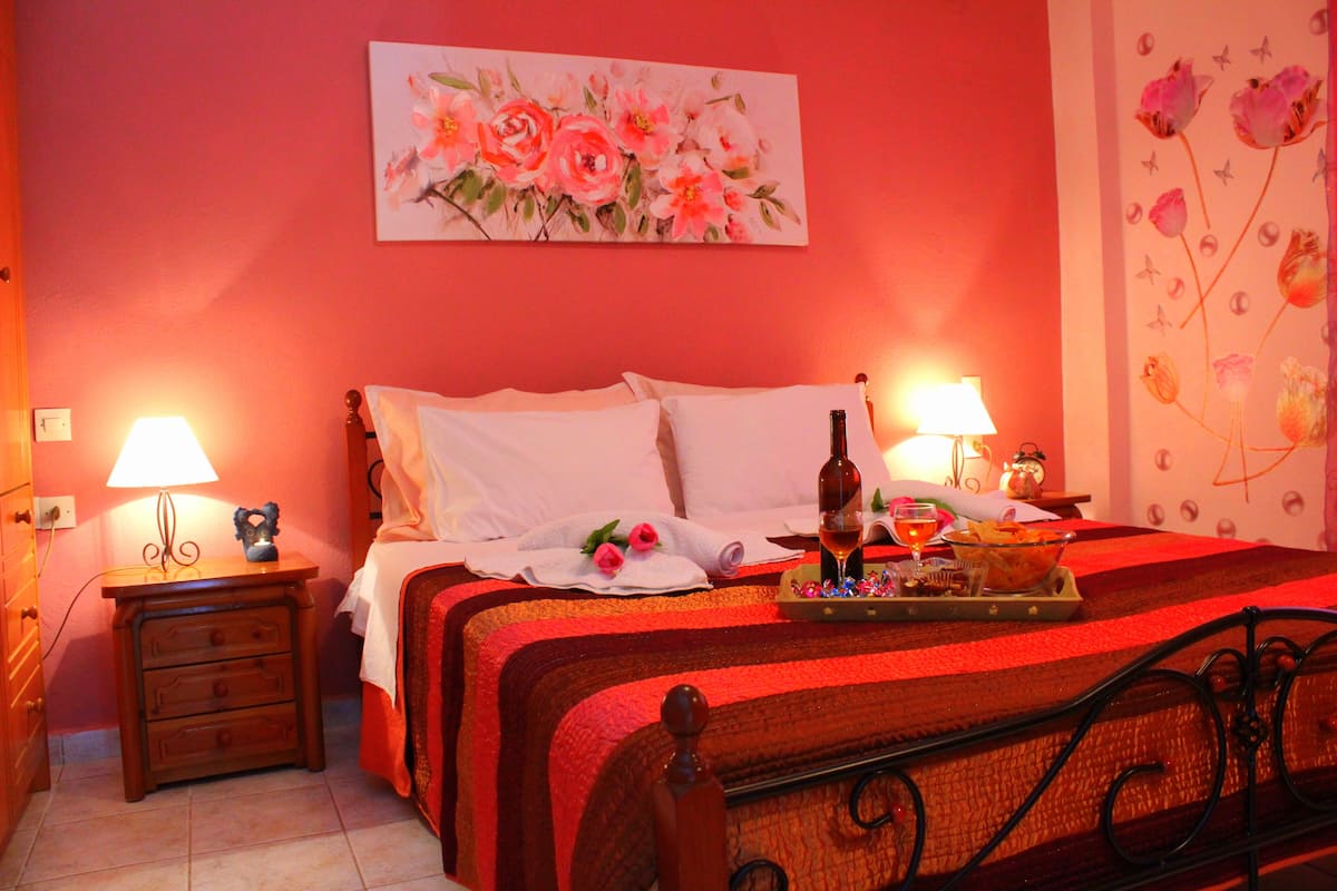 A hotel room with a bed, two bedside tables with lamps, a painting on the wall, and a floral wallpaper on the right wall.
