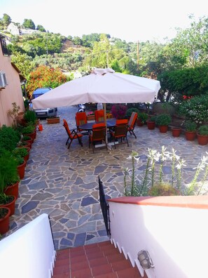 An outdoor patio with stone flooring, a table with chairs, and a large umbrella. - Tzaneria Apartments (Skiathos)