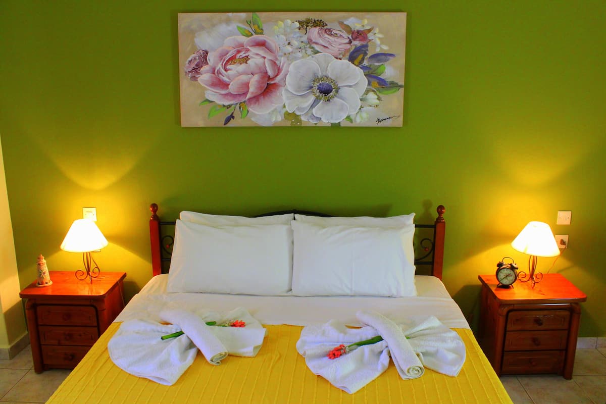 A hotel room with a bed, two bedside tables with lamps, a painting of flowers on the wall, and towels on the bed.