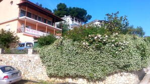 A multi-story building with a balcony, a stone wall, and a car parked in front.