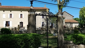 Un bâtiment en pierre doté d’une façade traditionnelle, d’une entrée fermée par un portail et d’un jardin bien entretenu.
