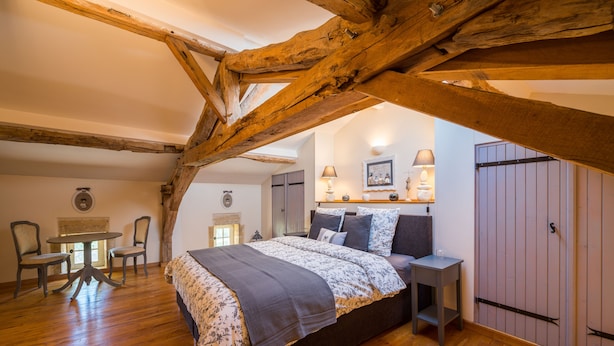 Une chambre avec un plafond en bois, un lit recouvert d’une couvre-lit à motifs floraux, une table de chevet avec une lampe et une armoire.
