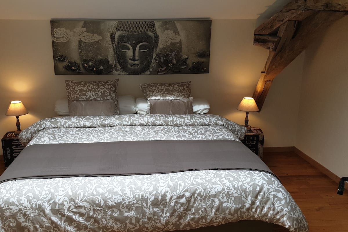 Un dormitorio con una cama grande, dos mesitas de noche, una obra de arte en la pared y una viga de techo de madera.