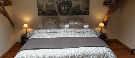 A bedroom with a large bed, two bedside tables, a wall-mounted artwork, and a wooden ceiling beam.