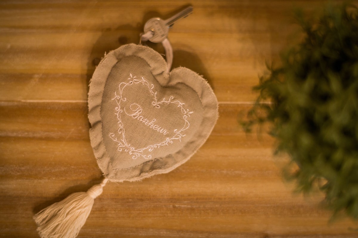 Decoración en forma de corazón con bordado y borla, colgando sobre una superficie de madera.