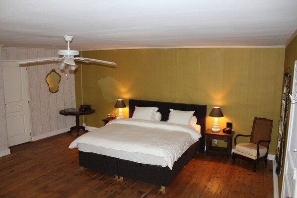 Un dormitorio con una cama, dos mesitas de noche, una silla, un ventilador de techo y un espejo en la pared.