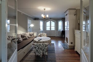 Una habitación con piso de madera, un sofá con cojines estampados, una mesa redonda y una silla, y una araña.