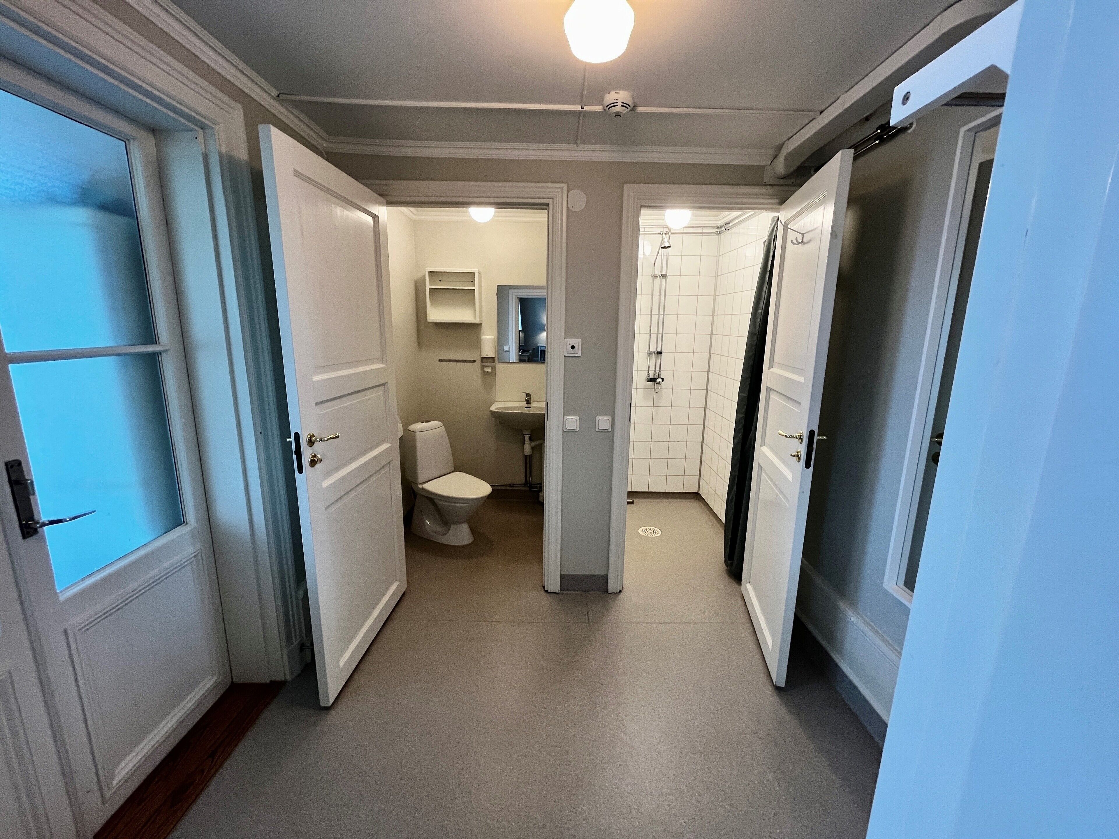 A narrow hallway leading to a bathroom with a toilet, sink, and shower.
