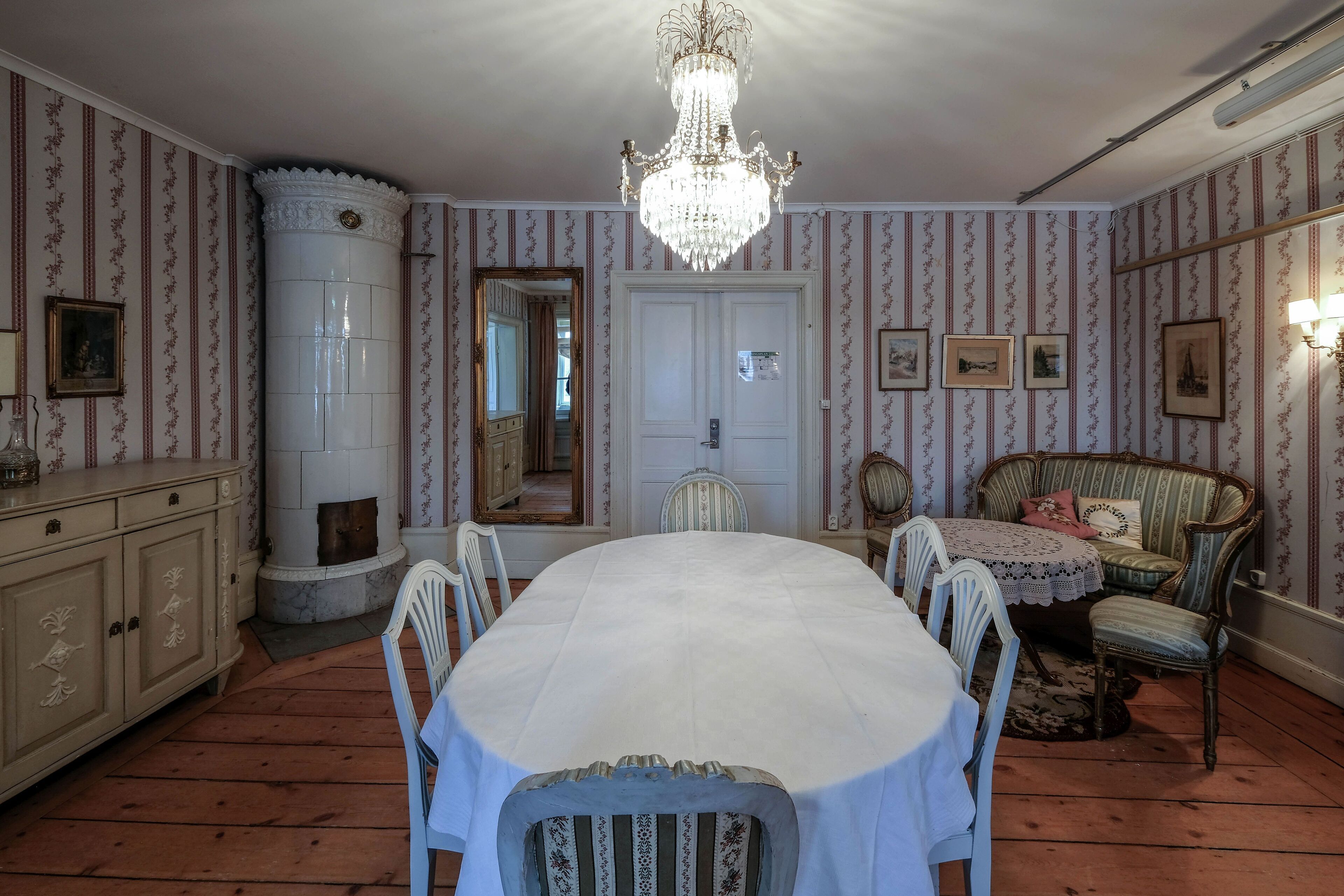 Ein Esszimmer mit großem Tisch, Stühlen, einer Chandelieber und einem Sofa.