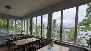 Comedor con amplias ventanas que dan a un lago, mesas y sillas de madera, y vistas de la vegetación circundante.