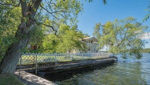 A wooden dock extending into a calm lake, surrounded by lush greenery and a white fence. - Klubbensborg (Hägersten)