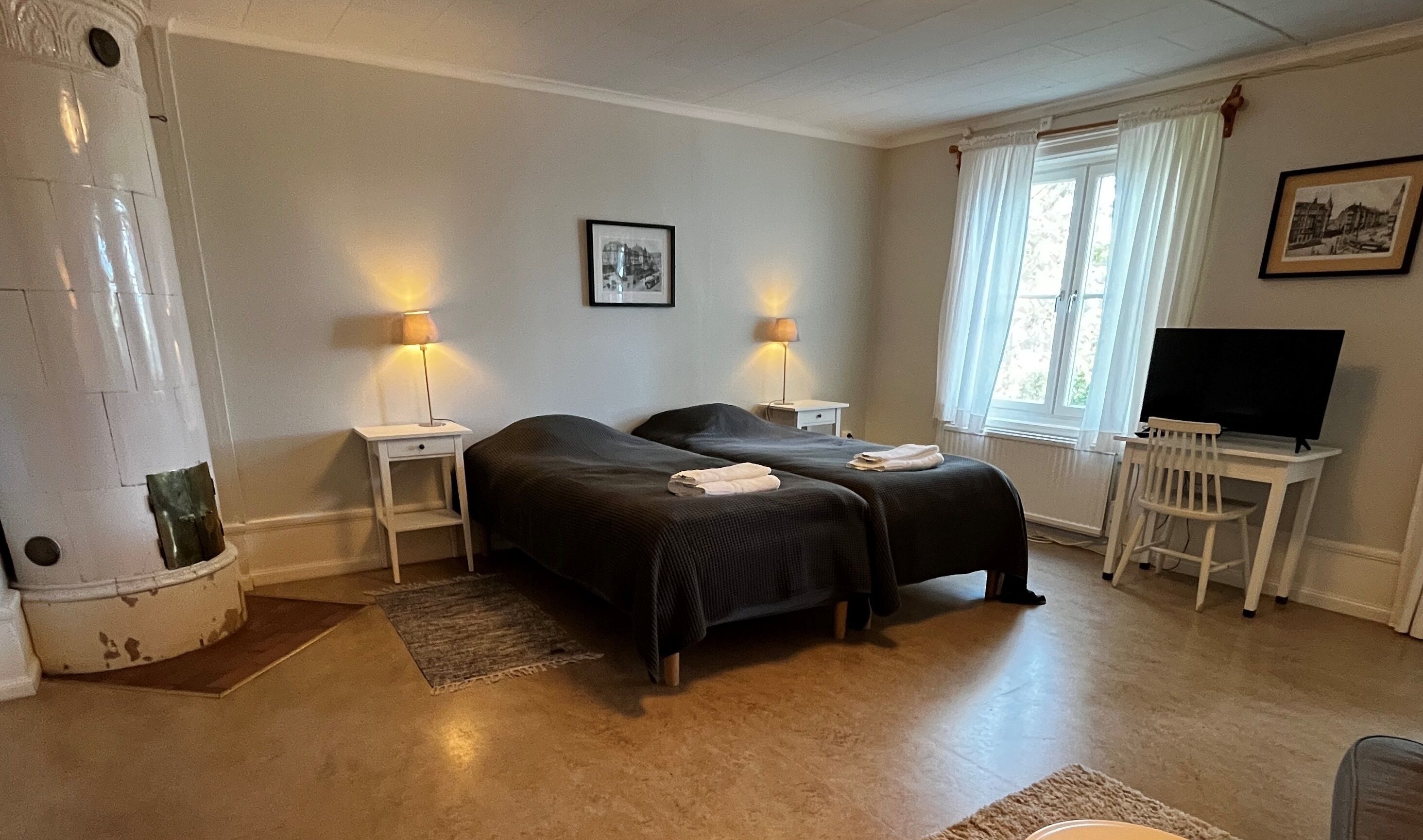 A hotel room with two beds, a desk with a chair, a television, and a window with curtains.
