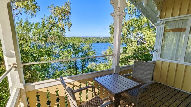 A wooden deck with a table and chairs, overlooking a lake and trees. - Klubbensborg (Hägersten)