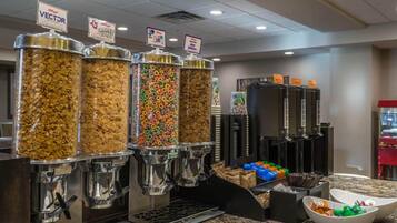 A breakfast bar with cereal dispensers, a coffee machine, and a bowl of fruit.