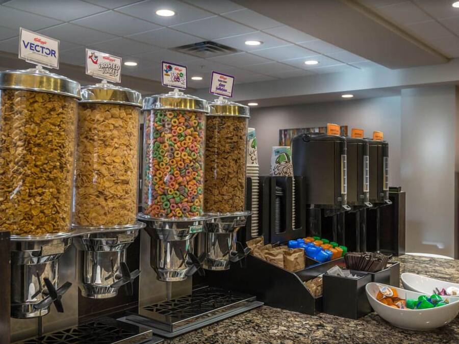 A breakfast bar with cereal dispensers, a coffee machine, and a bowl of fruit.