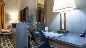 Une chambre d’hôtel équipée d’un bureau, d’une chaise, d’une télévision, d’une lampe et d’un miroir.