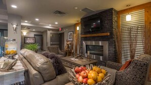 A modern living room with leather sofas, a stone fireplace, and a television mounted above it. - Timber Ridge Inn and Suites (Fox Creek)