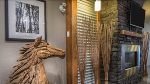 A rustic interior with a stone fireplace, a framed black and white forest photograph, and a wooden sculpture. - Timber Ridge Inn and Suites (Fox Creek)