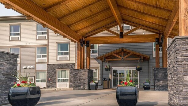 A covered outdoor area with a wooden roof, stone walls, and large planters with flowers. - Timber Ridge Inn and Suites (Fox Creek)