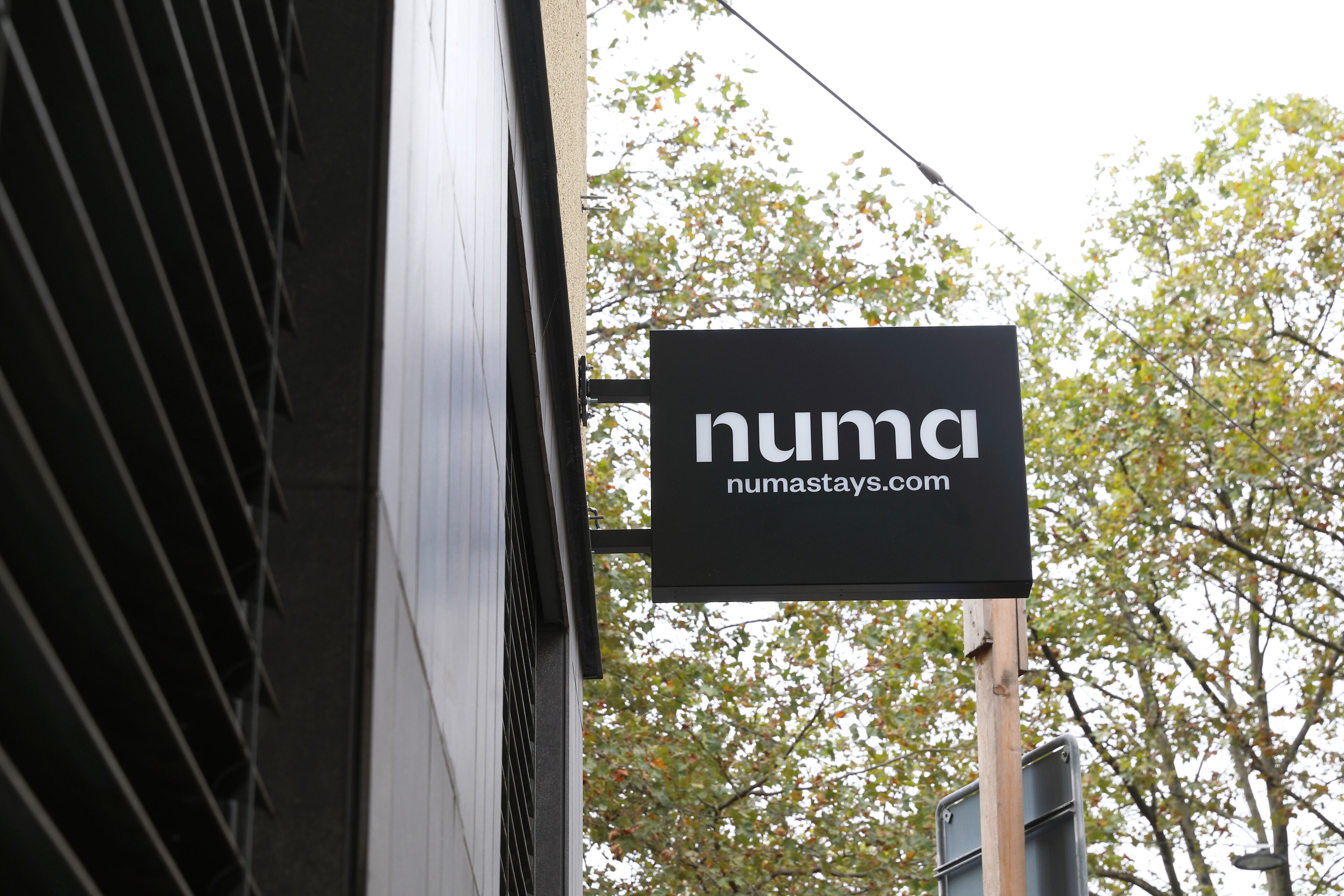 A black sign with white text reading "numastays.com" mounted on a building.