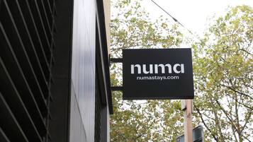 A black sign with white text reading "numastays.com" mounted on a building.
