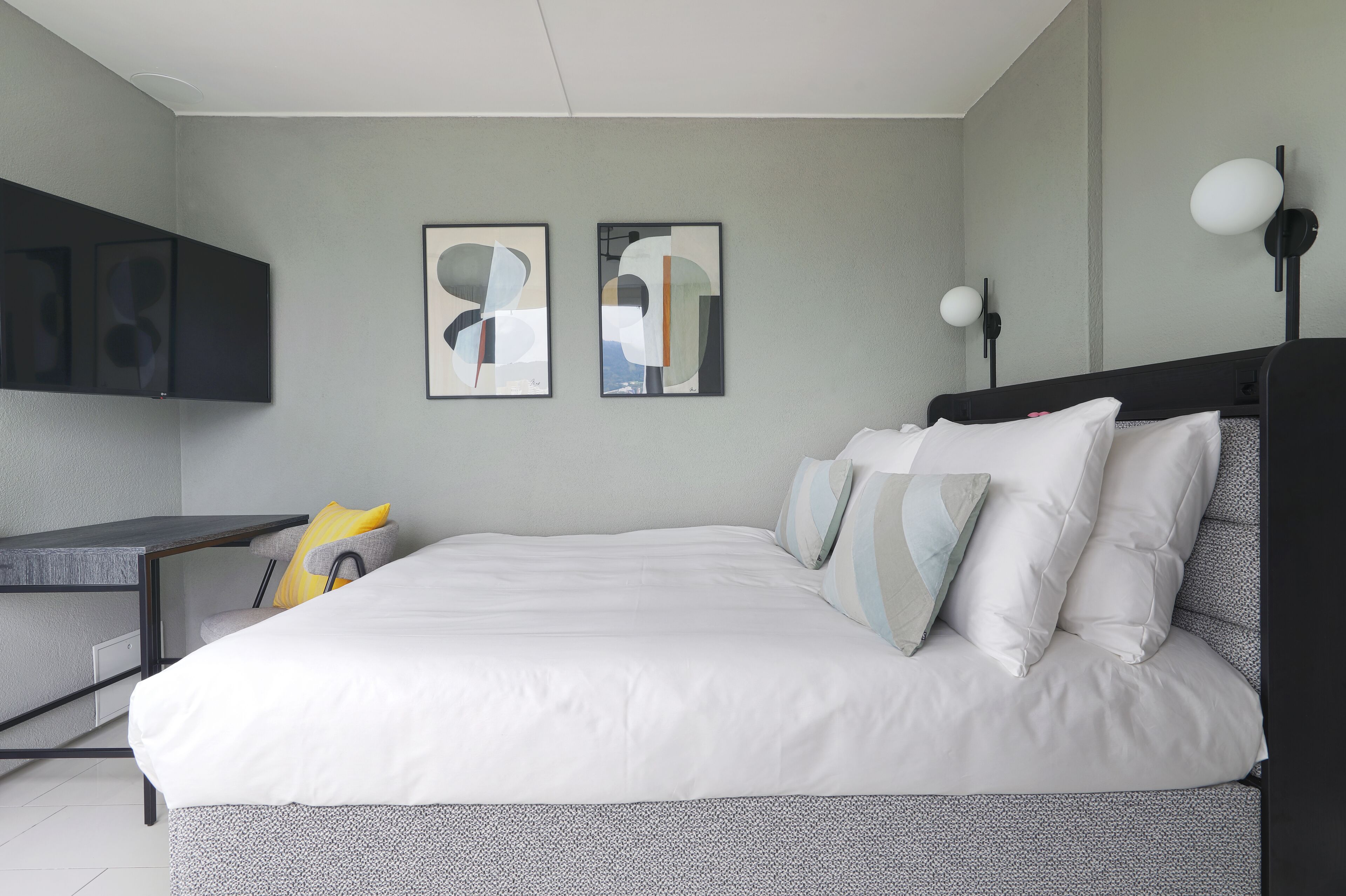 Quarto moderno com cama, escrivaninha e duas pinturas abstratas na parede.