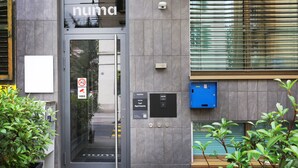 A modern building entrance with a glass door, a security camera, and a blue numbered sign. - Numa Zurich Turi (Zürich)