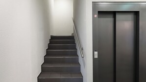 A staircase with a metal handrail leading to a dark elevator door. - Numa Zurich Turi (Zürich)