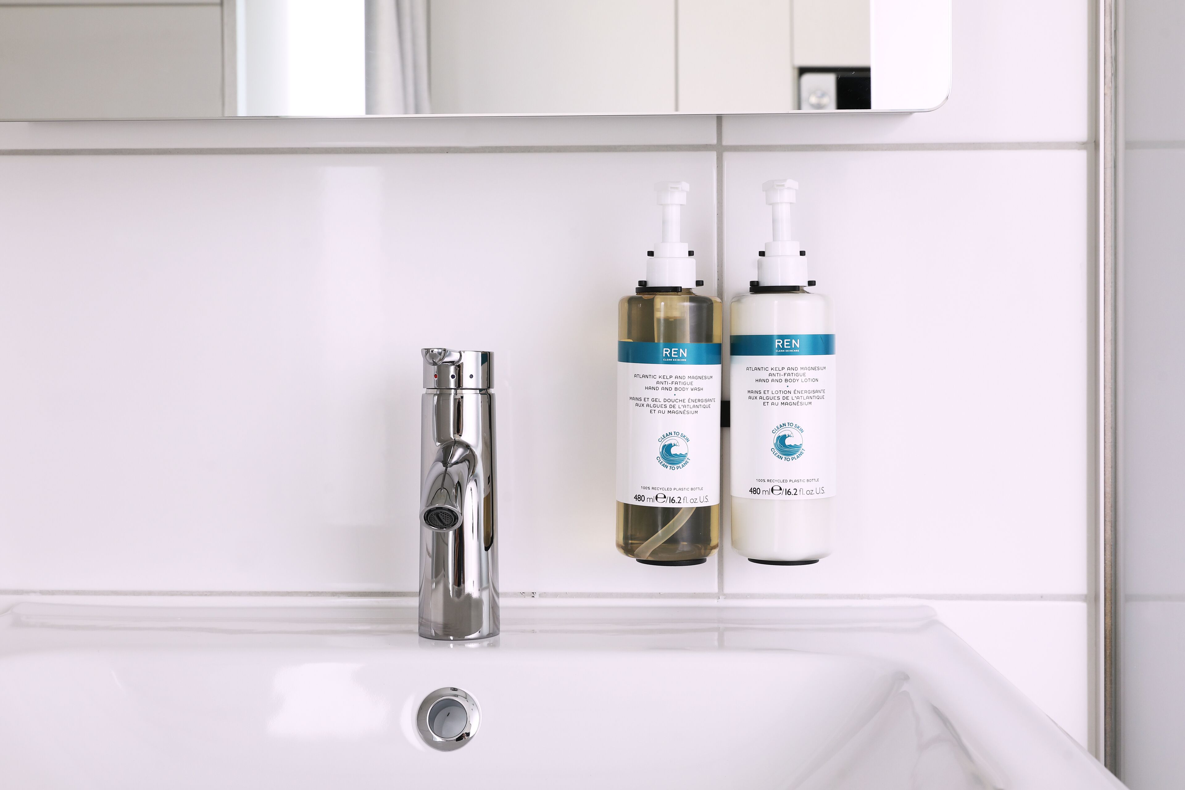 A bathroom with a white sink, a chrome faucet, and two bottles of REN body wash on the wall.