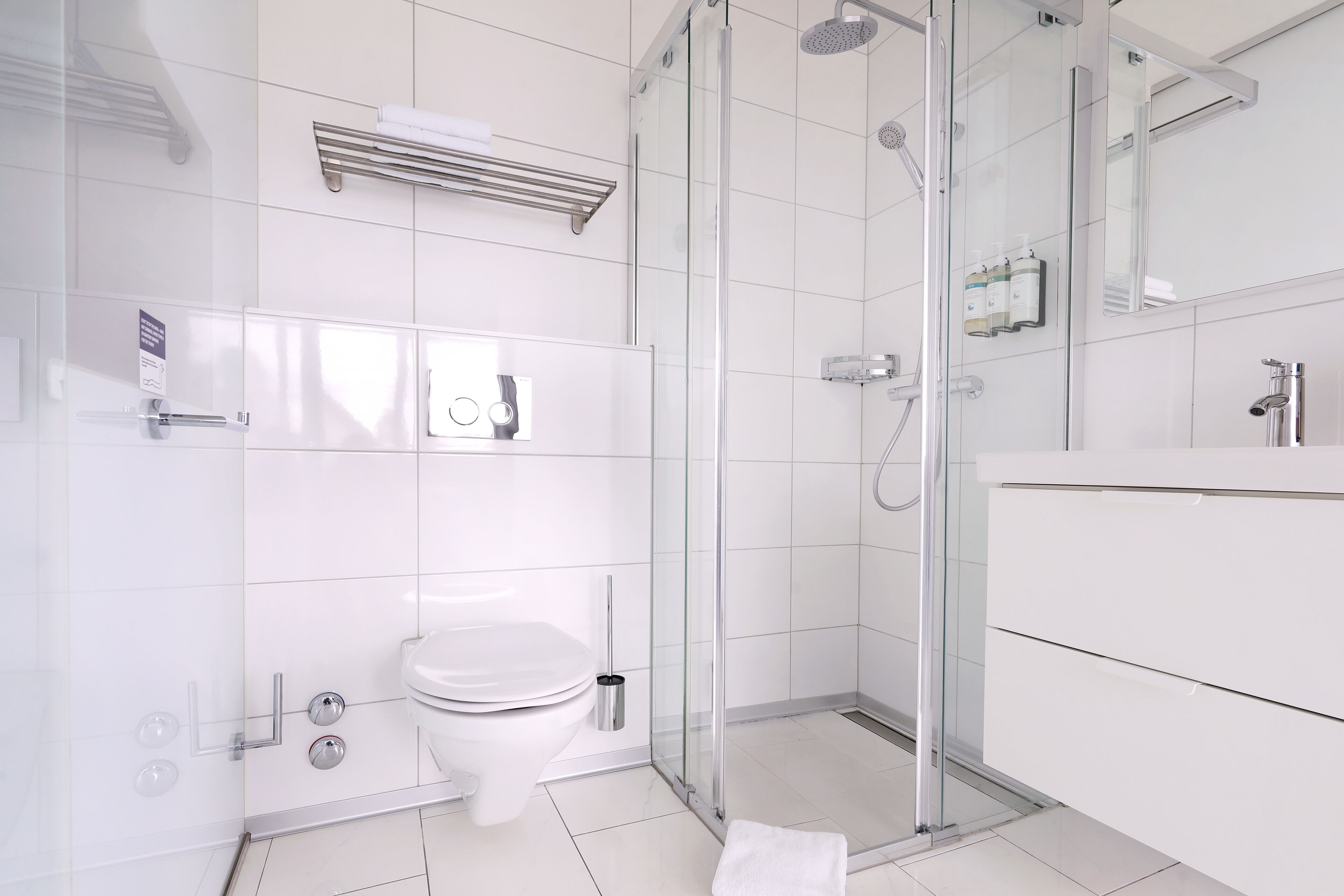 Une salle de bain moderne avec une douche à parois de verre, des toilettes blanches et un meuble-lavabo avec un miroir.
