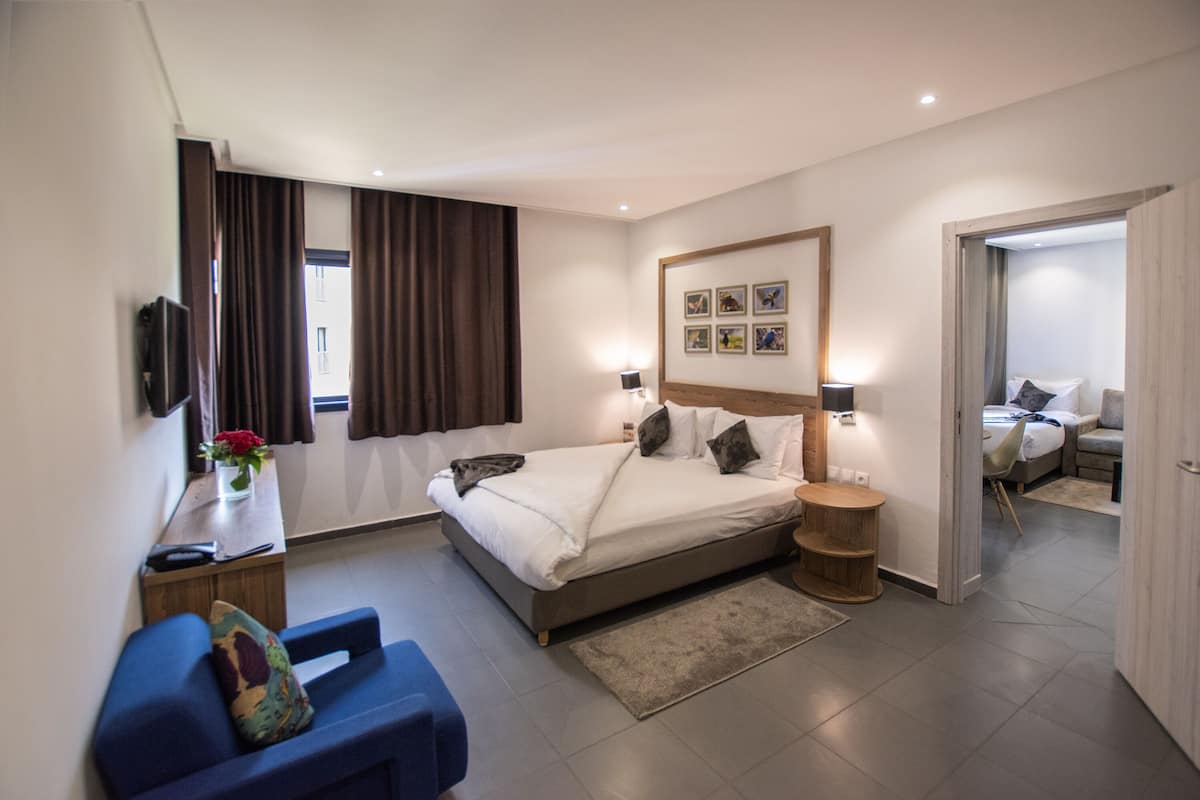 A modern hotel room with a large bed, a desk with a chair, a small table, and a TV.