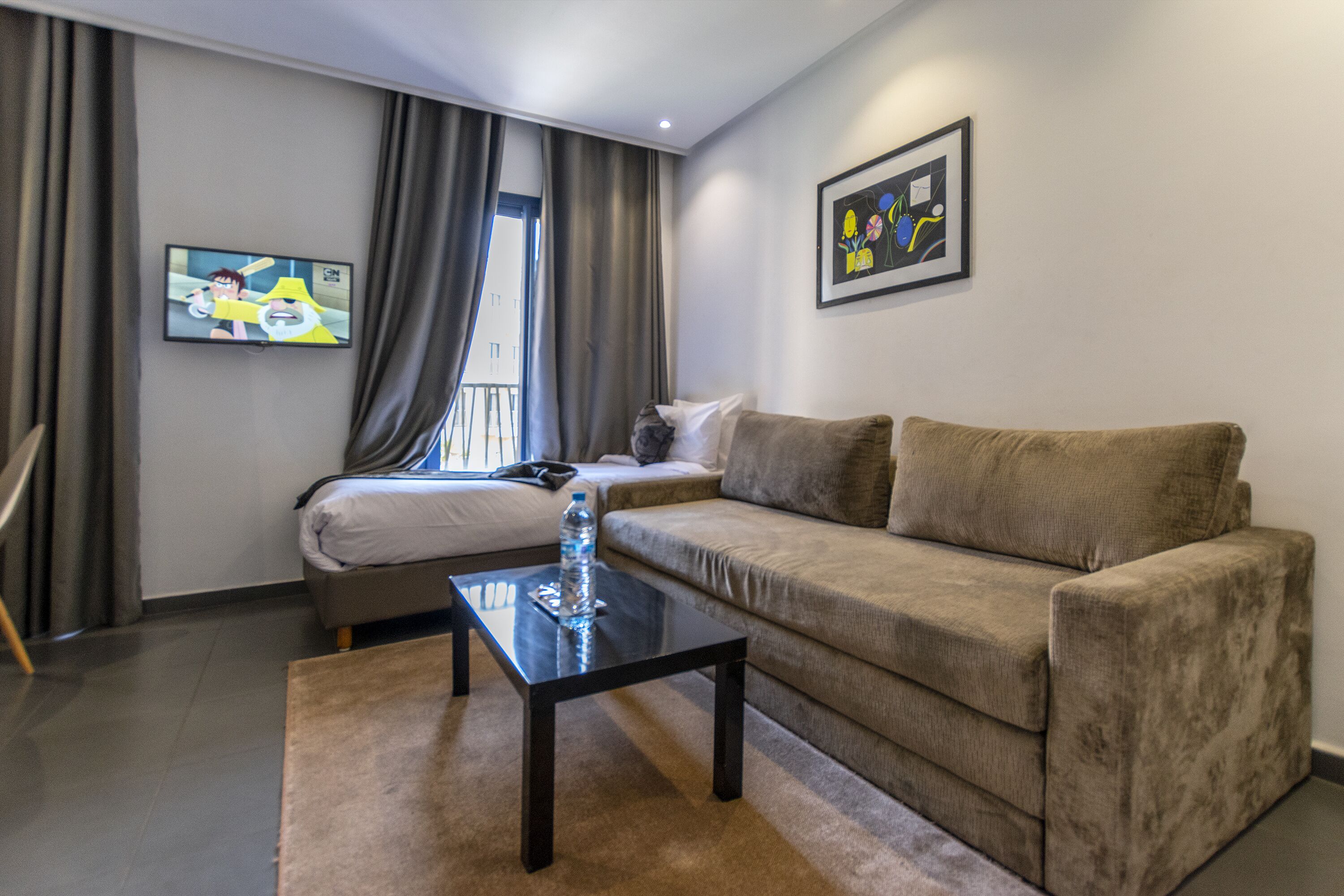 Una sala de estar moderna con un sofá, una mesa de centro, un televisor montado en la pared y una ventana con cortinas.