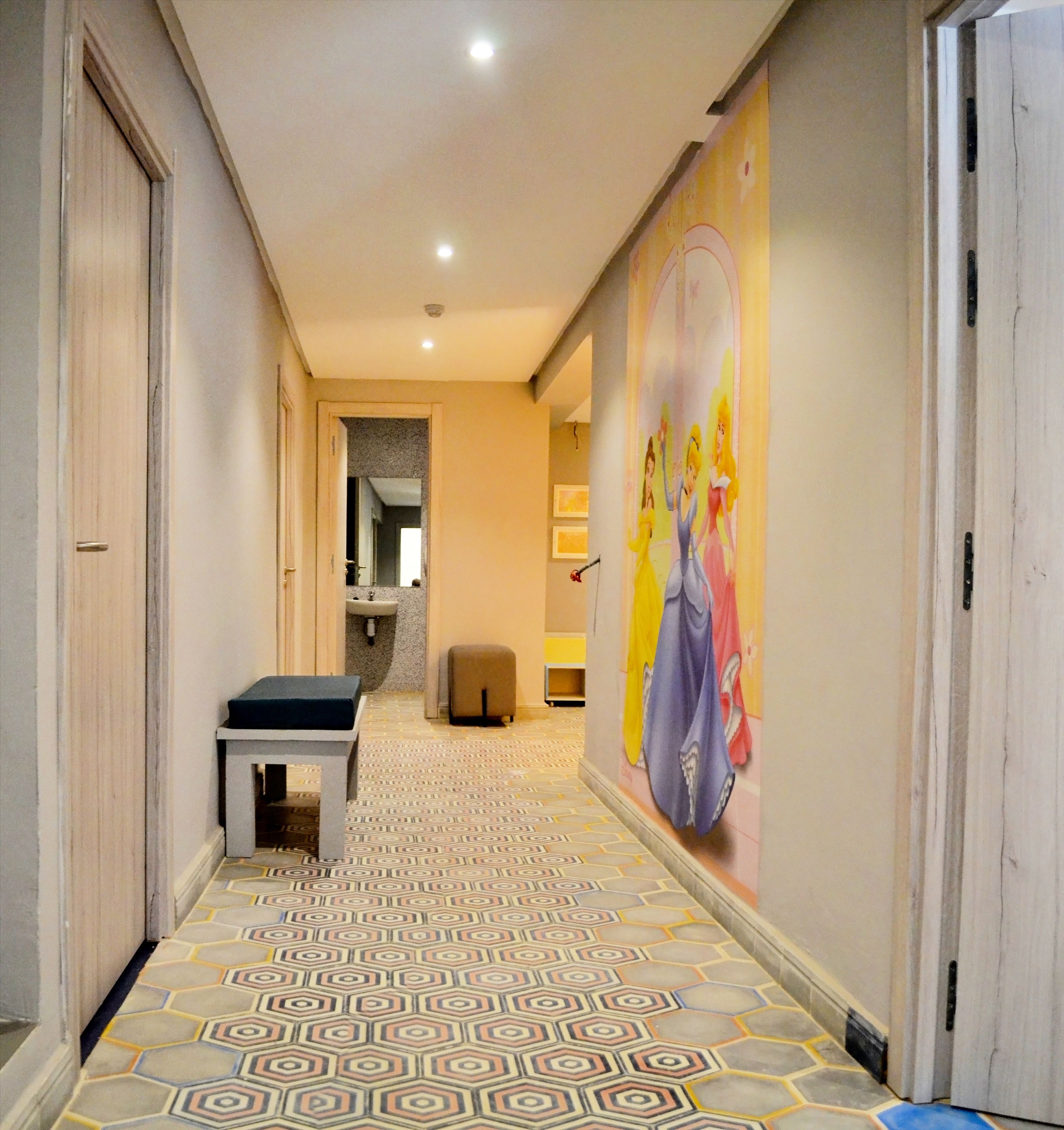 A hallway with patterned flooring, a bench, a wall mural, and a door on the right.