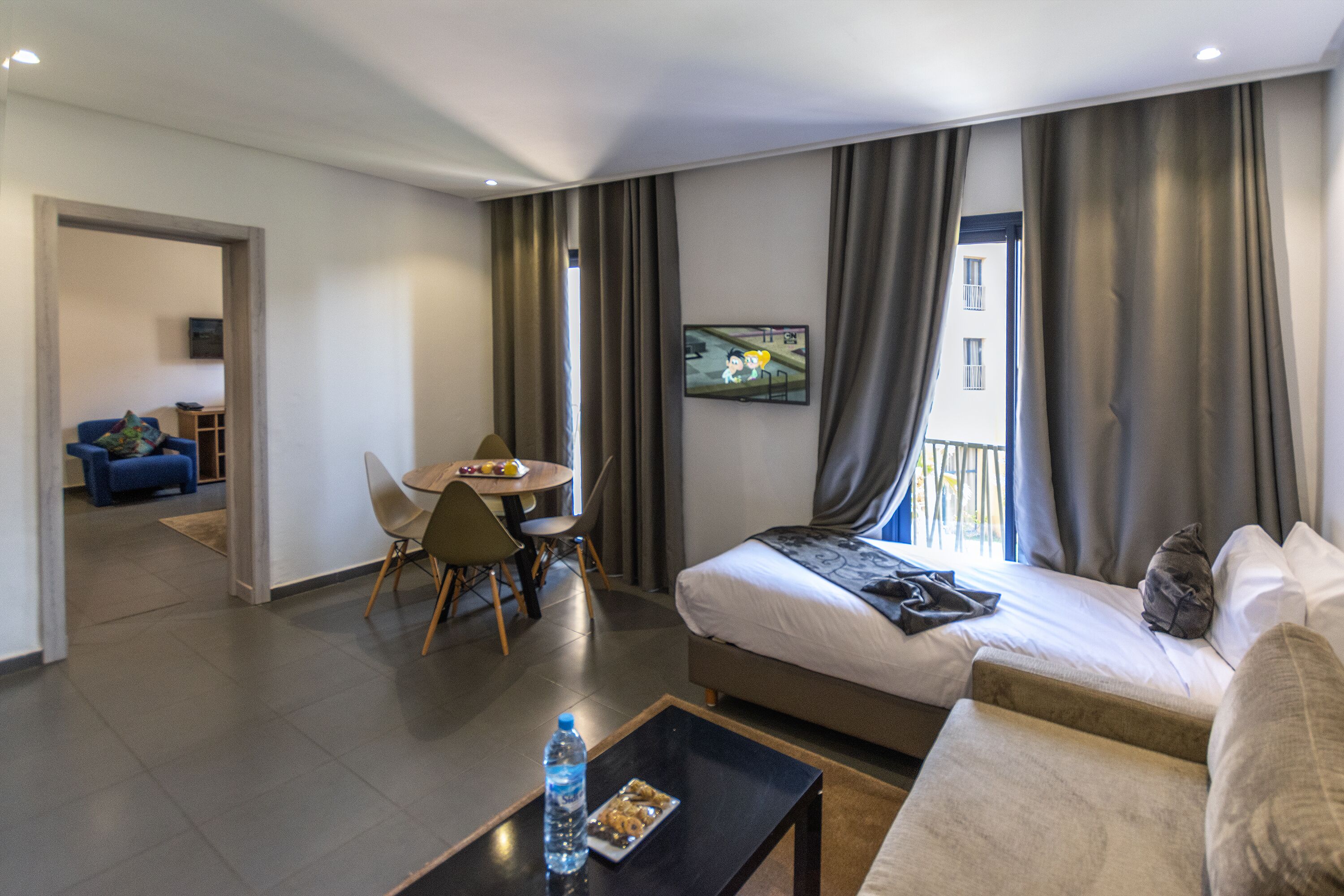 Una habitación de hotel moderna con una cama, un sofá, una mesa de comedor con sillas y un televisor montado en la pared.