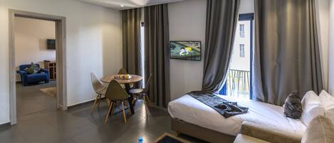 Una habitación de hotel moderna con una cama, un sofá, una mesa de comedor con sillas y un televisor montado en la pared.
