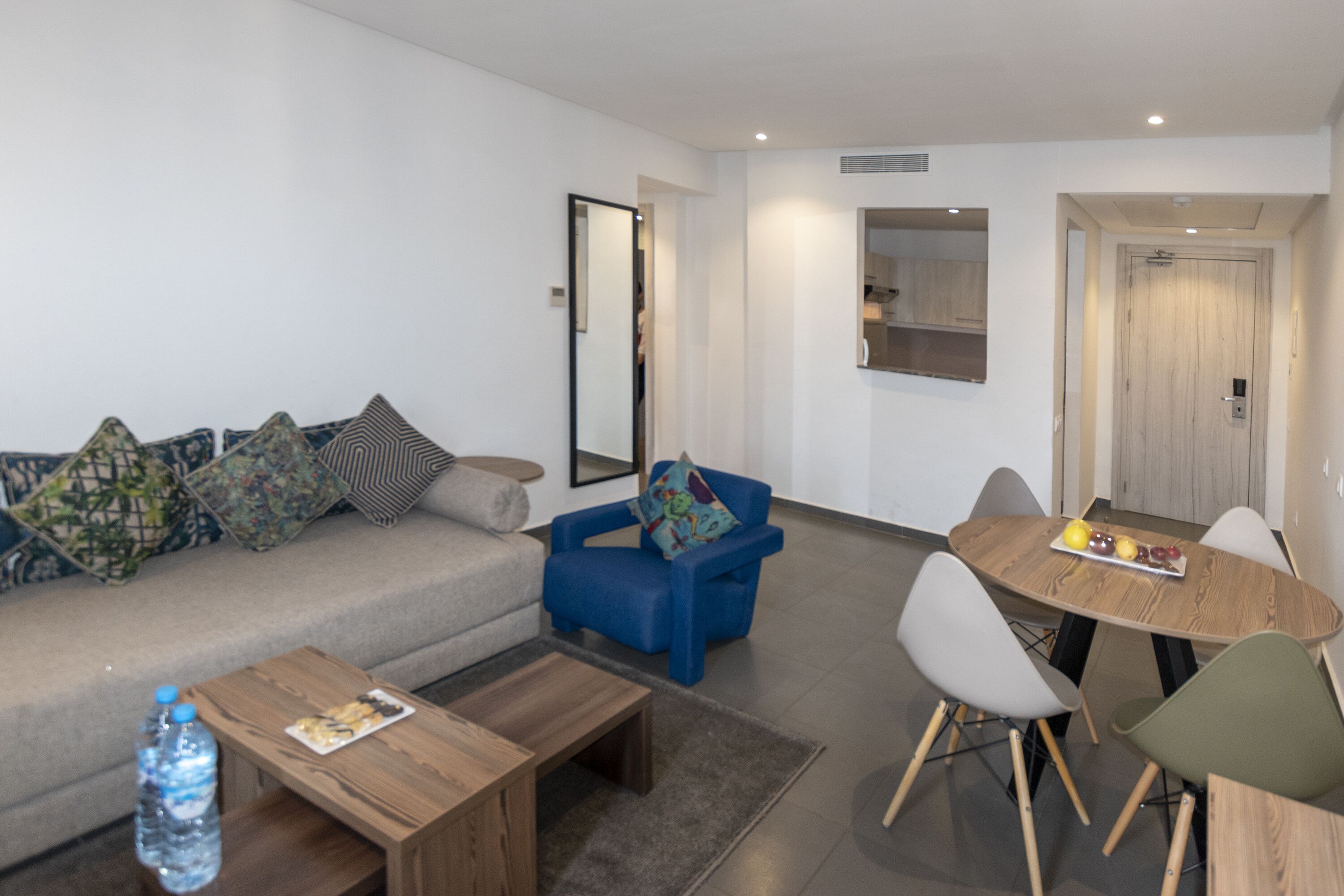 Uma sala de estar moderna com sofá, poltrona azul, mesa de centro de madeira e um espaço de jantar com mesa e cadeiras de madeira.