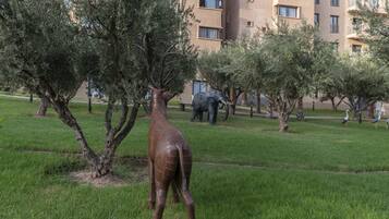 A sculpture of a giraffe in a grassy area with trees and a building in the background.