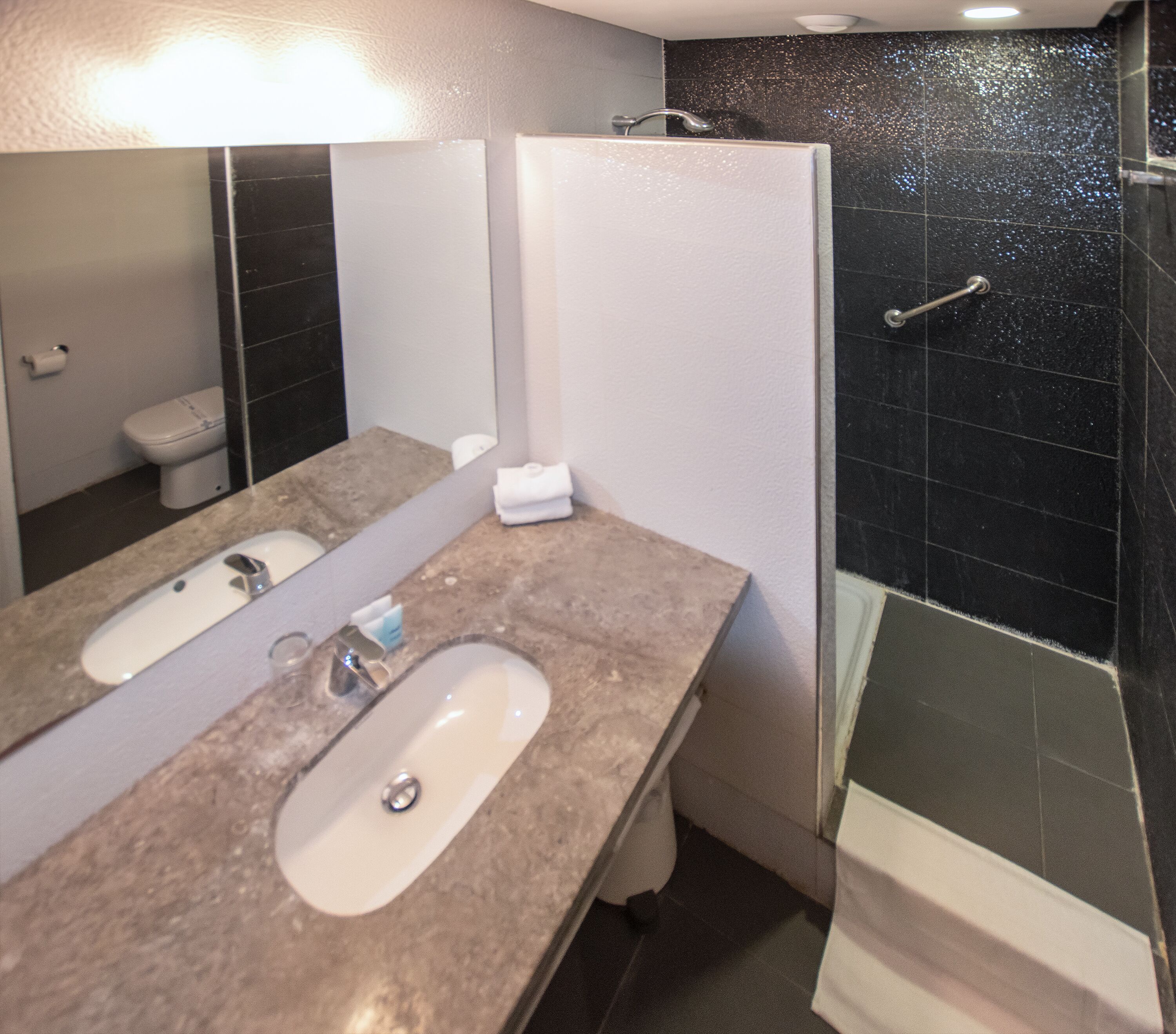 Une salle de bain avec un double lavabo, un miroir, un porte-serviettes et un espace douche.