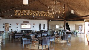 A spacious living area with a high ceiling, a fireplace, and a variety of seating arrangements including sofas and chairs. - Mbalageti Serengeti (Bariadi)