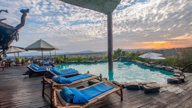 A wooden deck with lounge chairs and umbrellas overlooking a pool and scenic landscape. - Mbalageti Serengeti (Bariadi)
