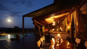 A wooden deck with a bar area, outdoor seating, and a pool. - Mbalageti Serengeti (Bariadi)