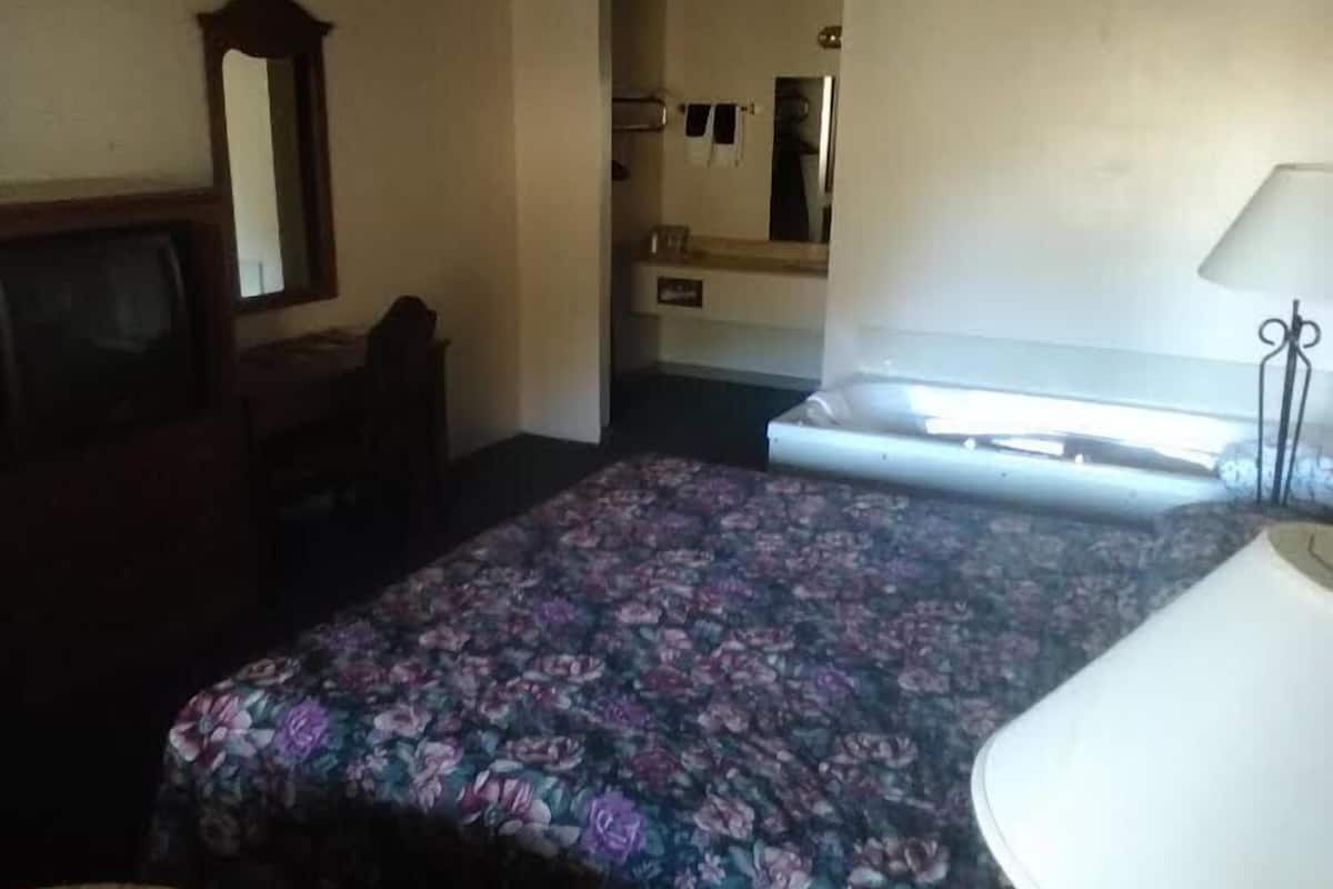 A room with a bed, a desk, a mirror, and a bathroom with a sink and towel rack.