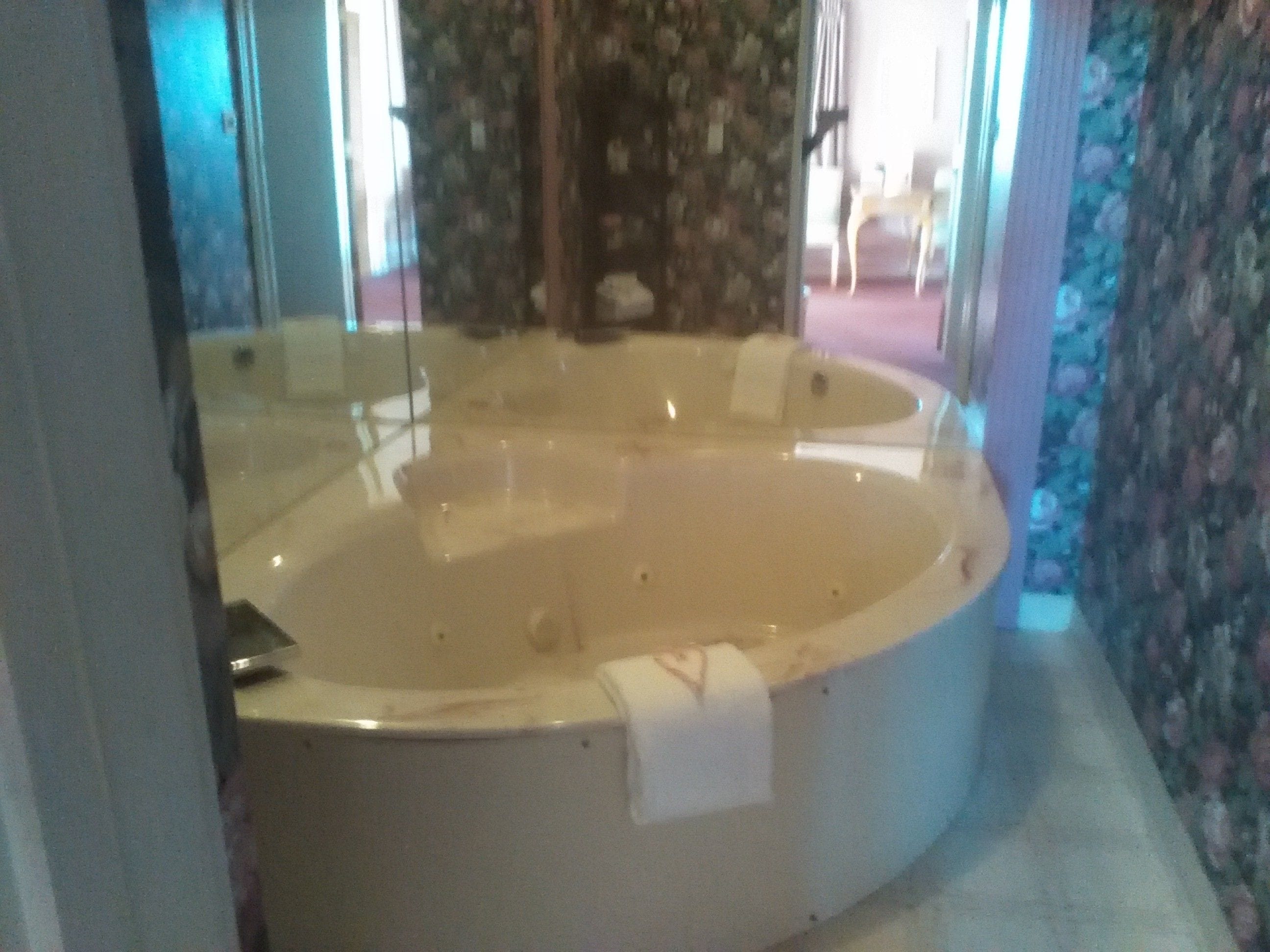 A bathroom with a large bathtub, a mirror, and floral wallpaper.