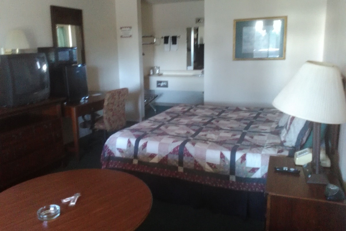 A hotel room with a bed, a desk, a chair, a TV, and a lamp.