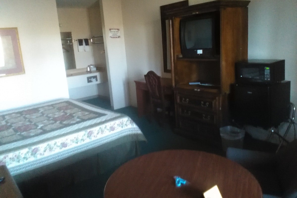 A hotel room with a bed, a small round table, a television, and a microwave.