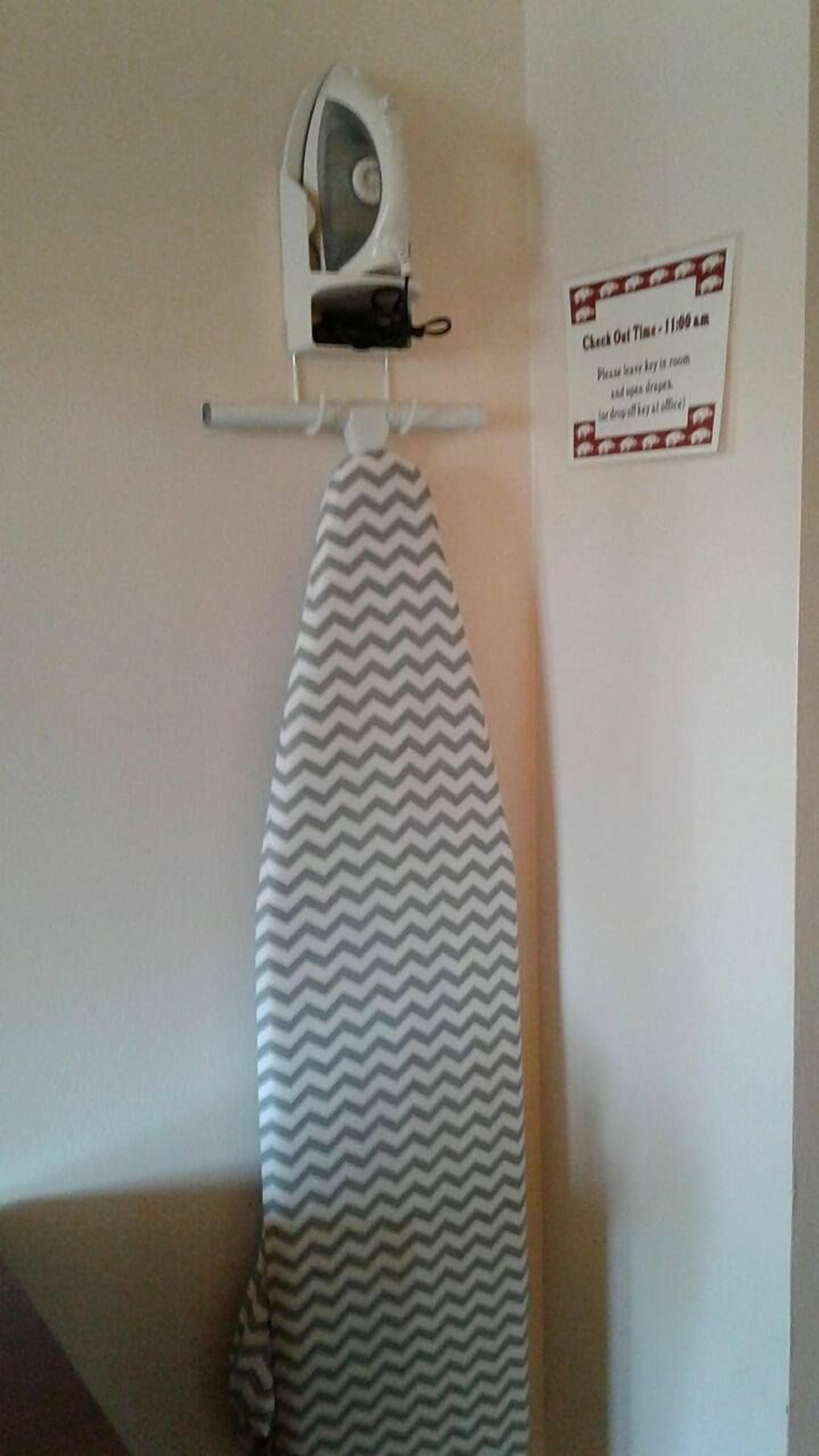 Tabla de planchar fijada a la pared, con un planchador y un aviso sobre la hora de salida.