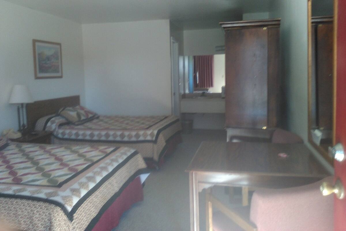 A hotel room with two beds, a desk, a chair, a wardrobe, and a mirror.
