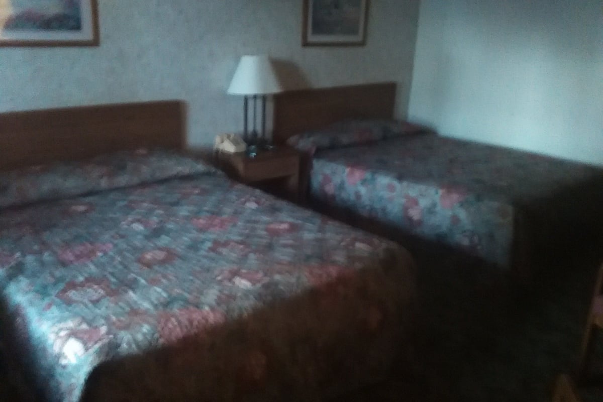 A hotel room with two beds, a nightstand, and a lamp.